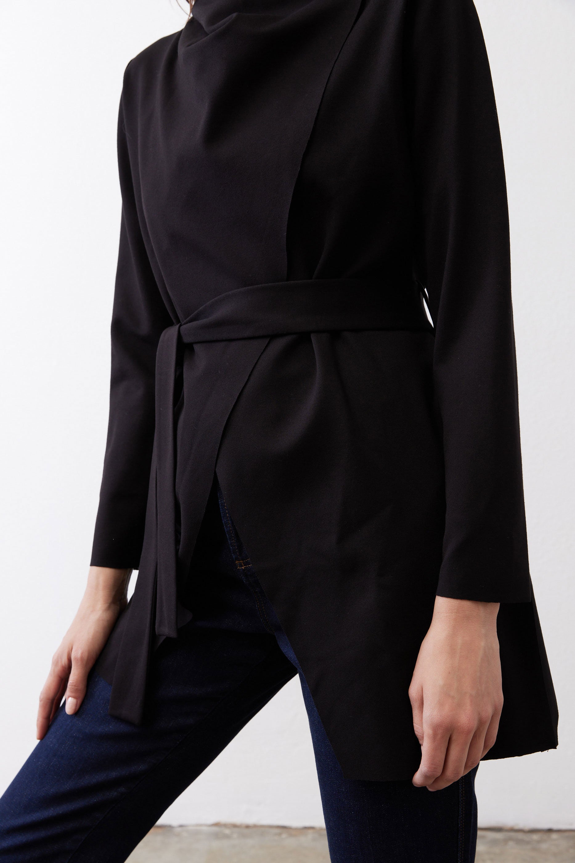 Black jacket close-up: tied waist belt and curved drape at hem.