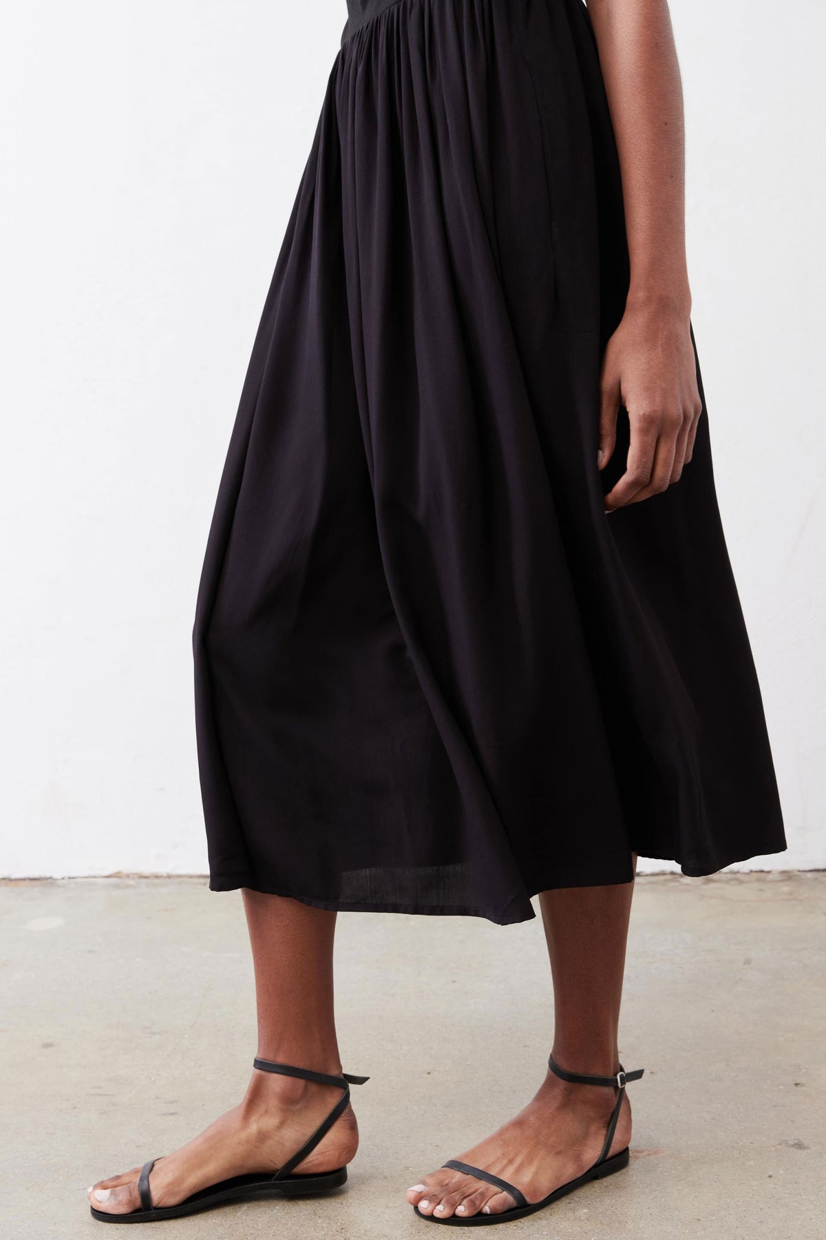 Black high-neck tank dress with gathered skirt, sleeveless midi hem detail