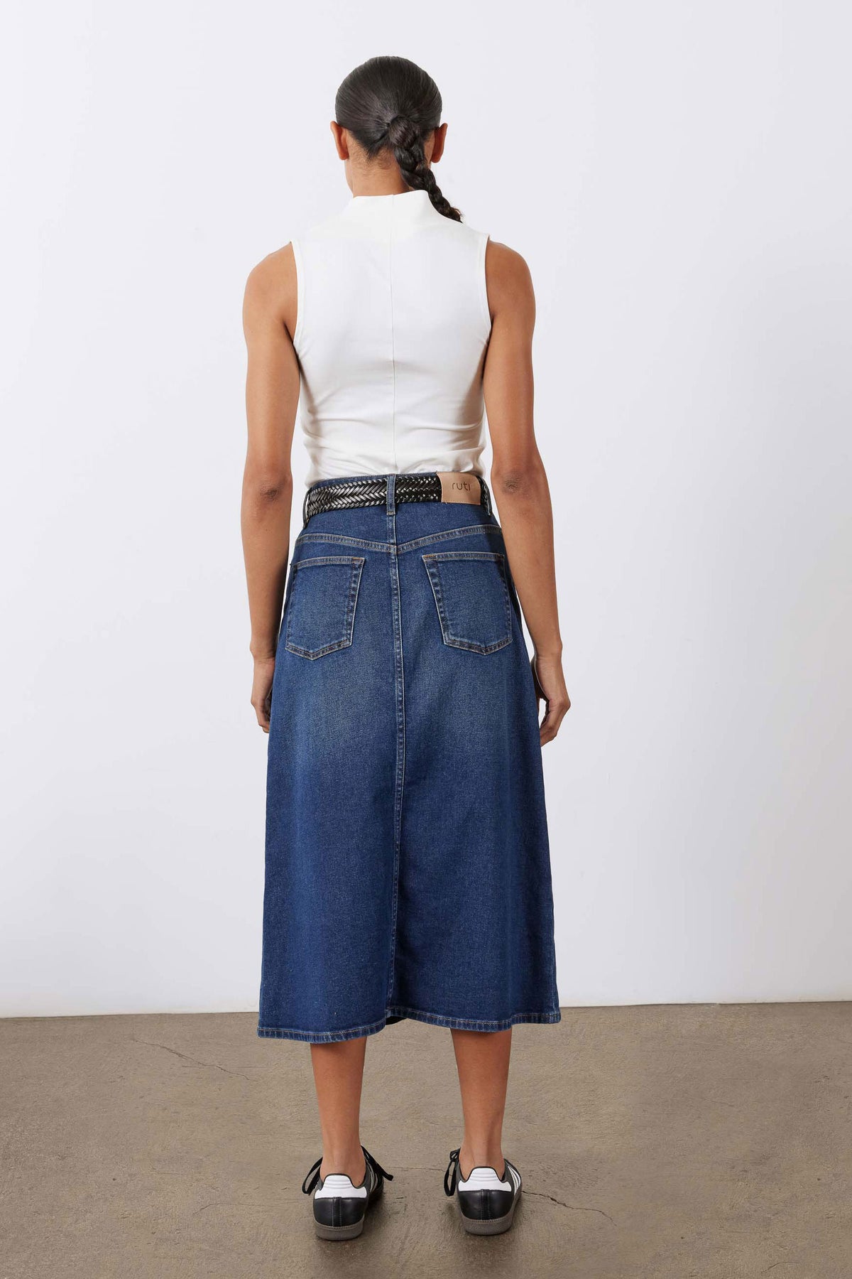 Women’s medium-wash denim midi skirt back view with belted waist and side pockets