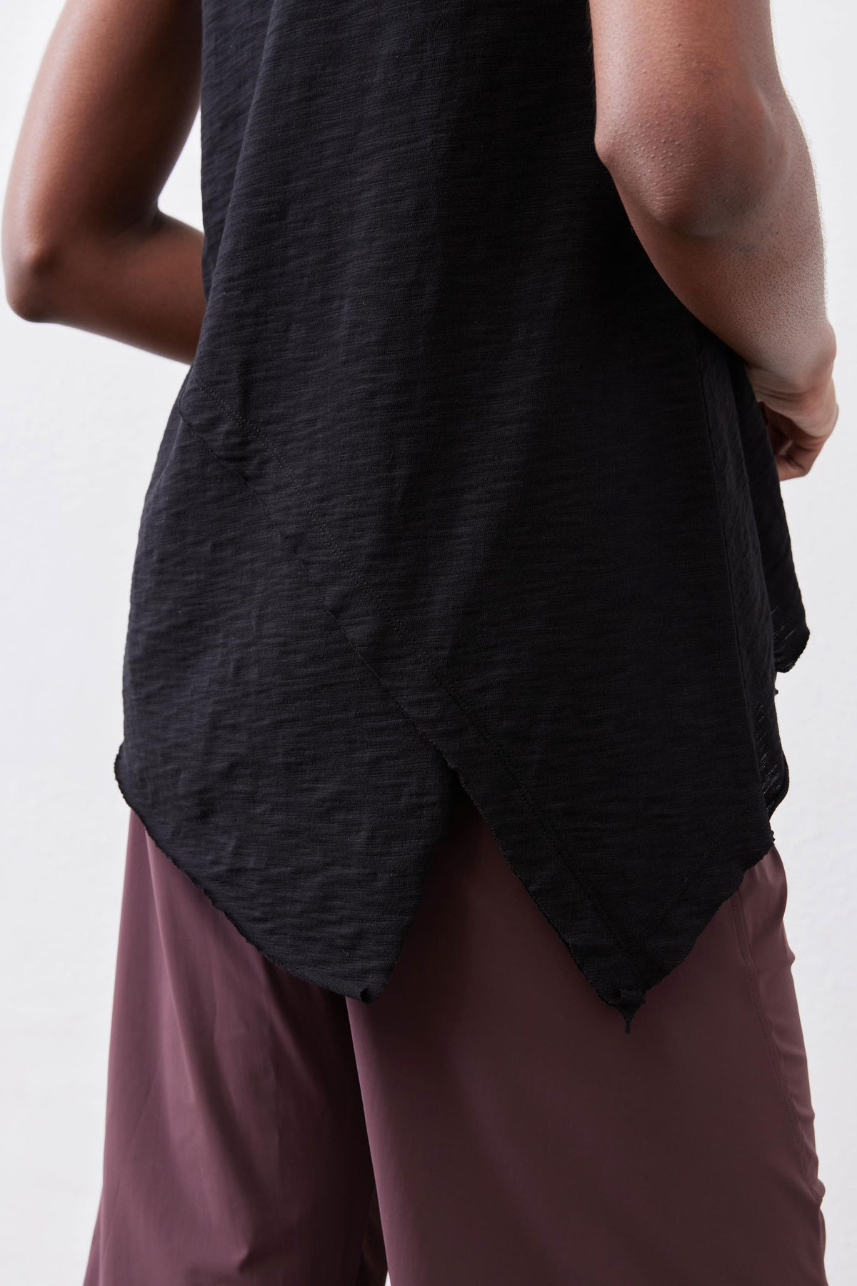 Black tank top showing curved, asymmetric draped hem over pants.