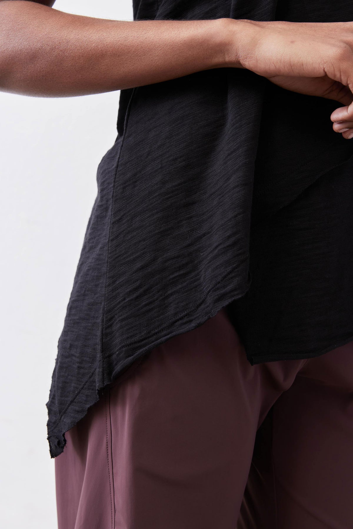 Black asymmetric tank hem overlap detail over mauve pants.
