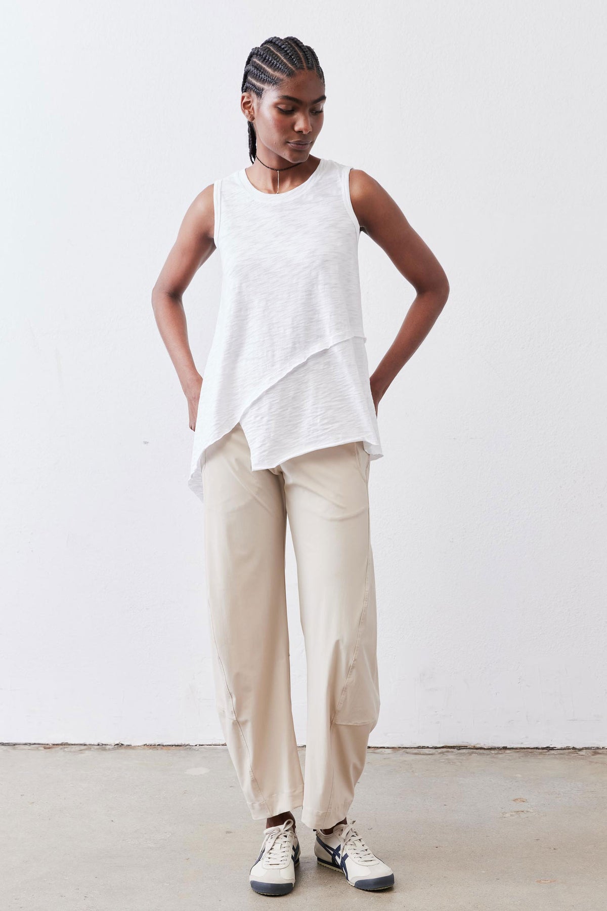 White asymmetric tank top with crew neck and uneven hem over beige pants