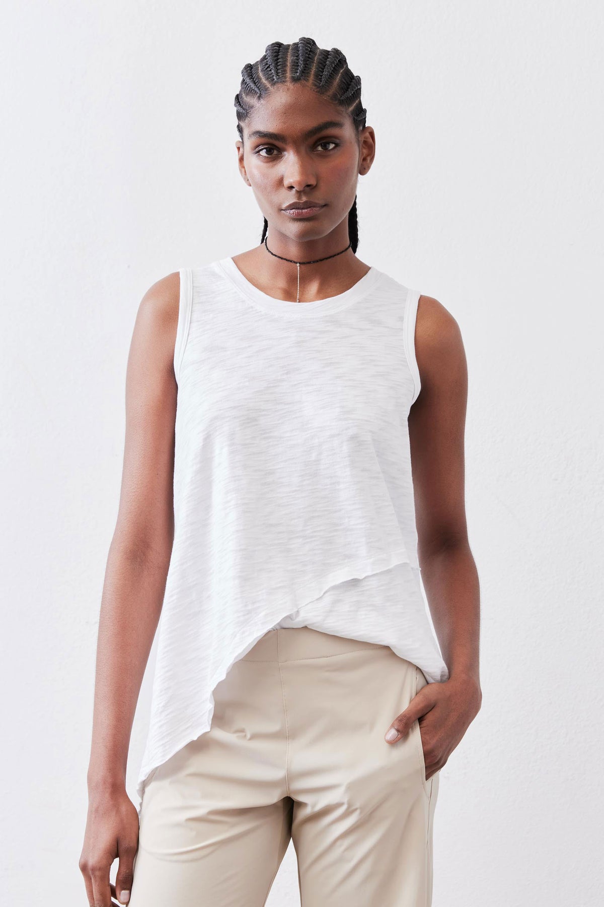 White sleeveless asymmetric tank with crew neck and uneven hem, worn with light pants