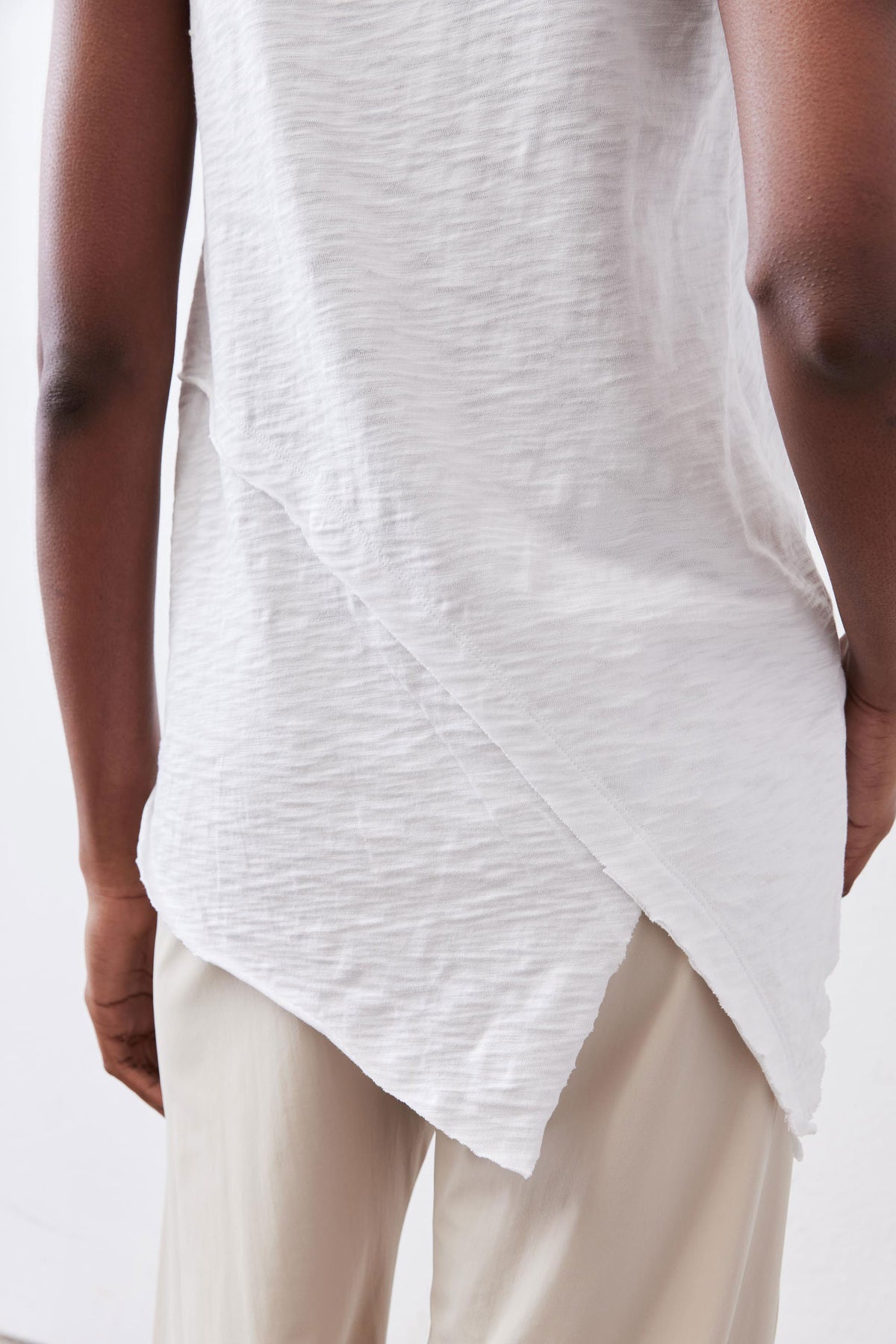 Close-up of white asymmetric tank hem and sleeveless armhole over beige pants