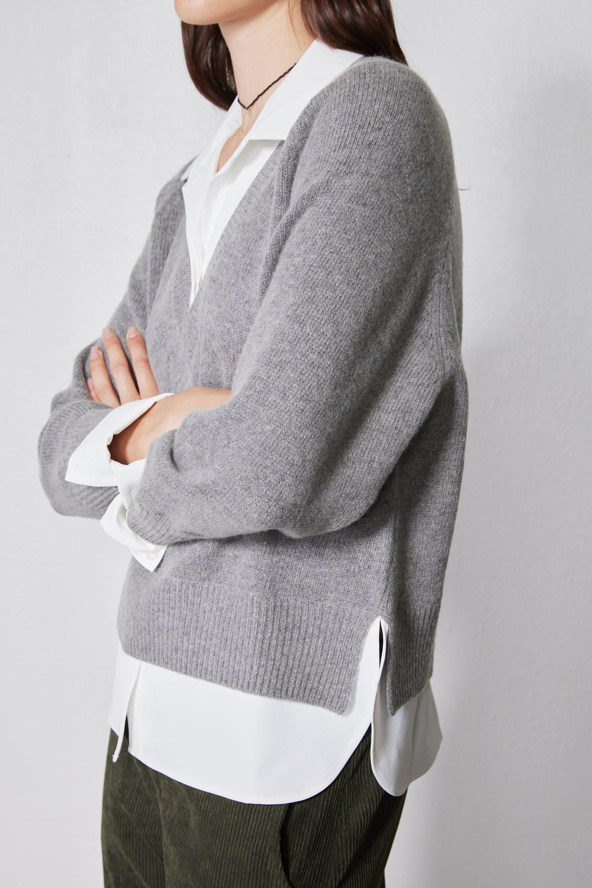 Side view of gray pullover sweater with white shirt underneath and buttoned cuff detail