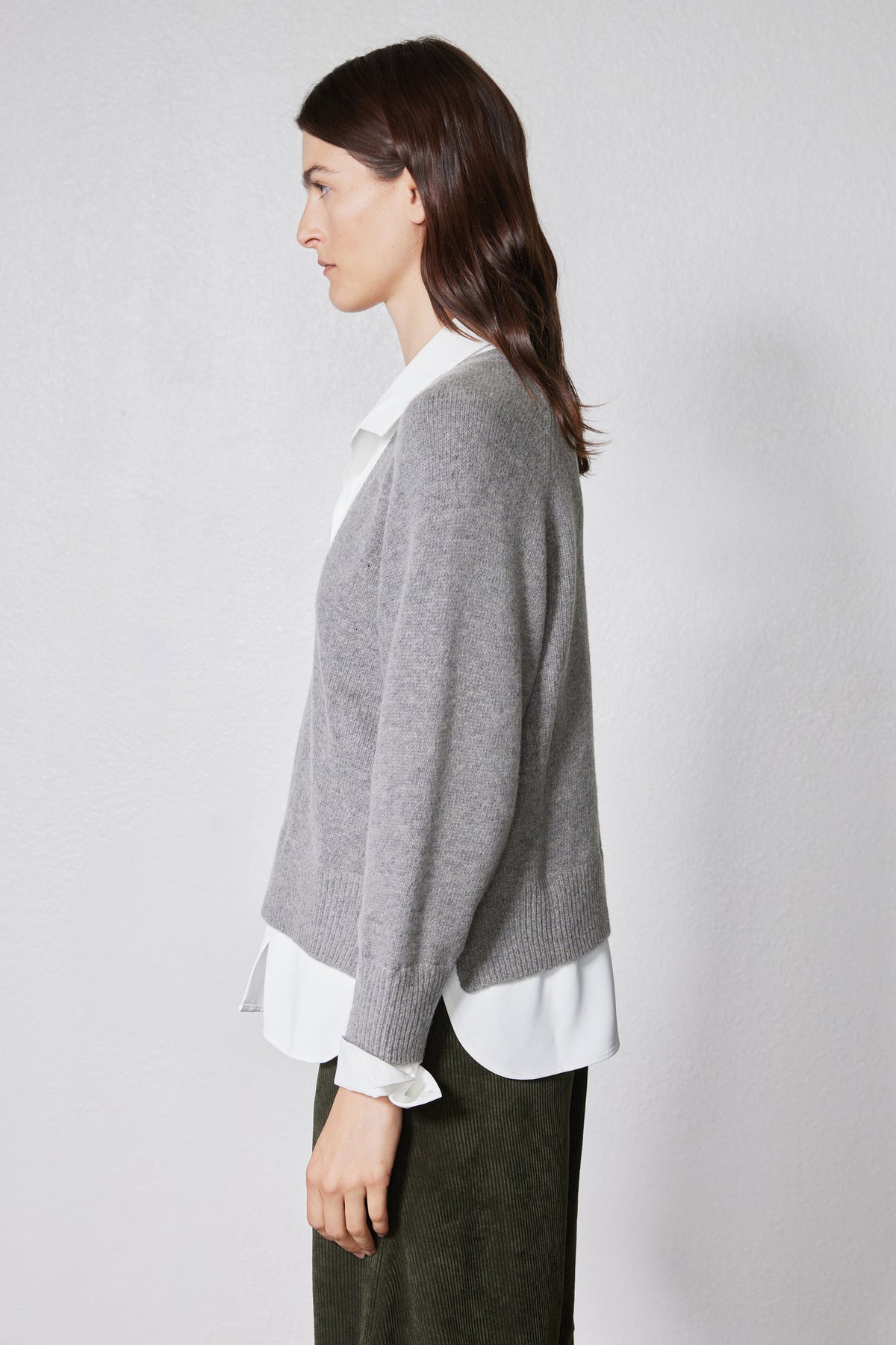 Gray knit pullover sweater in side profile with white shirt hem peeking below
