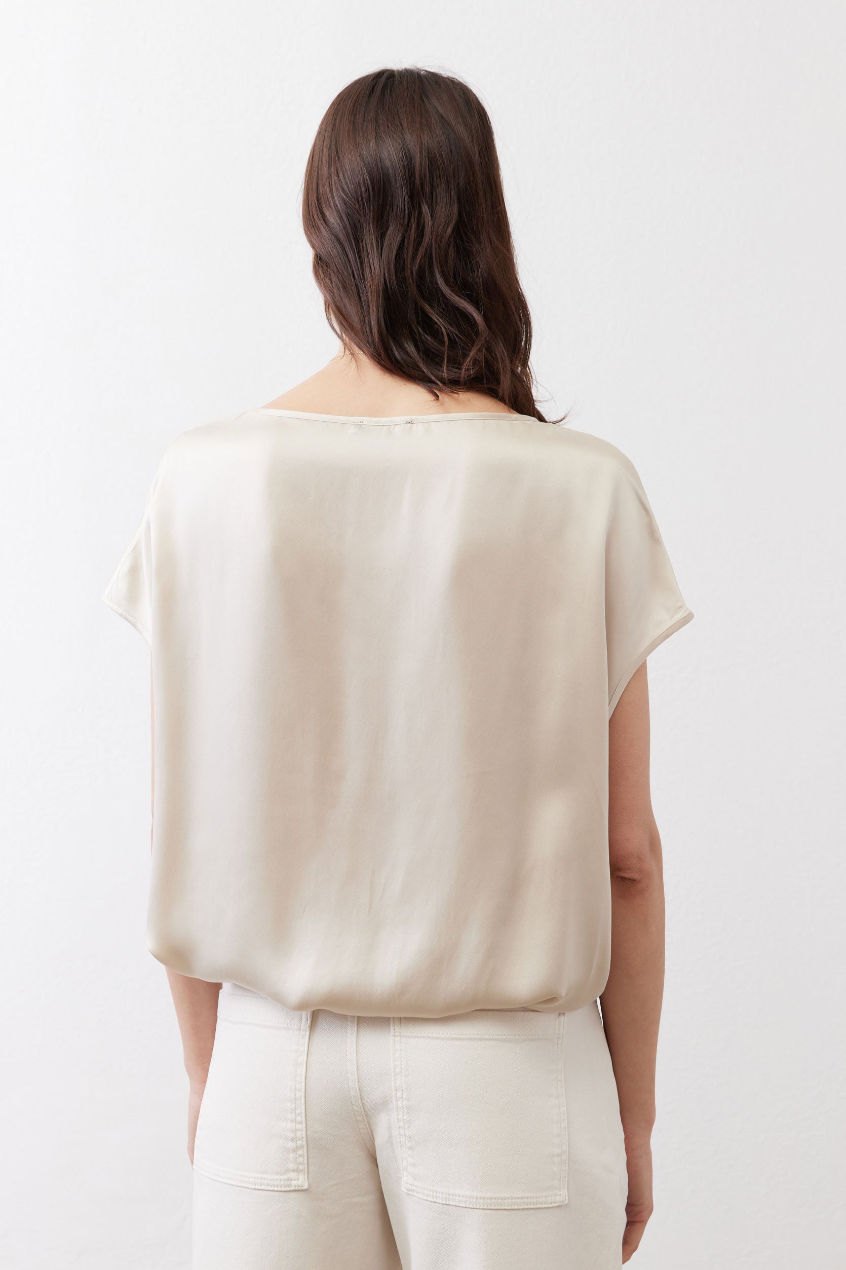 Off-white silk blouse back view with short sleeves, draped over light pants