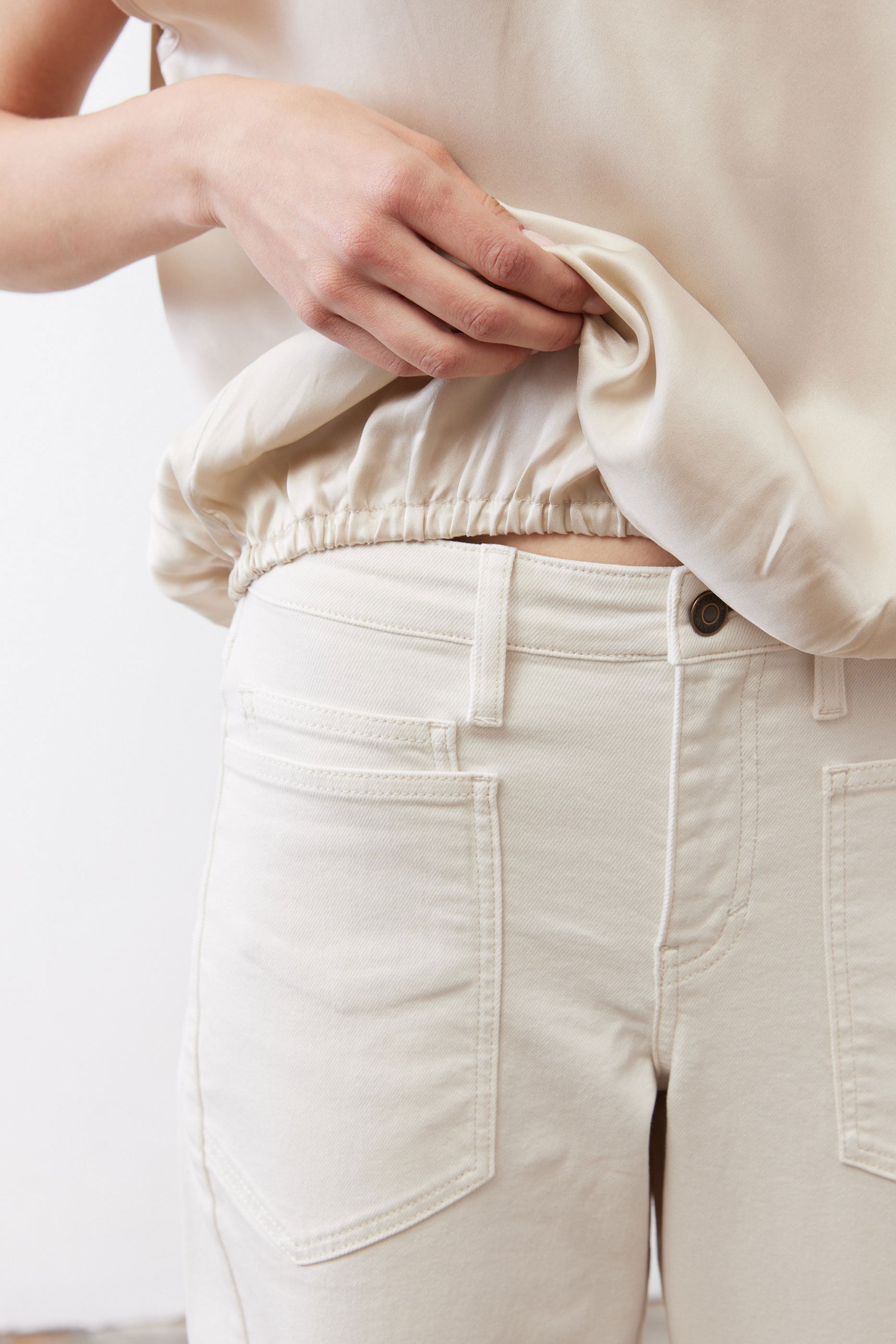 Off-white silk blouse sleeve and gathered hem detail over light pants