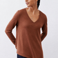 Brown V-neck long-sleeve top with draped, curved hem over dark jeans