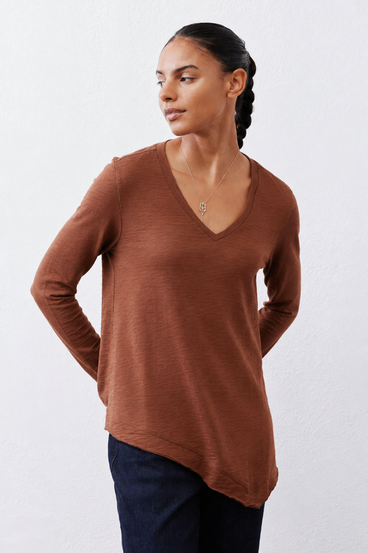 Brown V-neck long-sleeve top with draped, curved hem over dark jeans