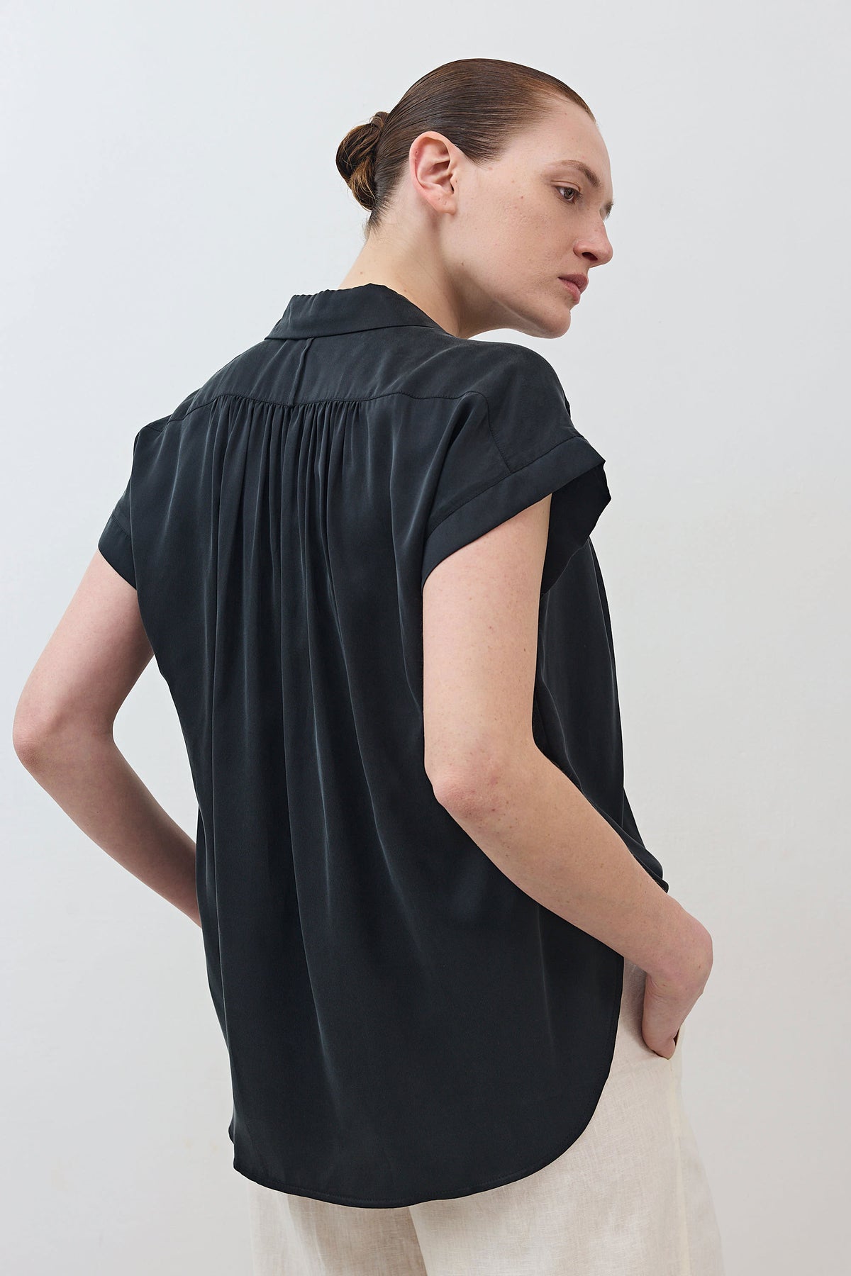 Back view of black oversized silk blouse with gathered yoke and short cap sleeves