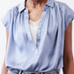 Steel blue silk blouse front with V-neck button placket and lace-trim neckline.