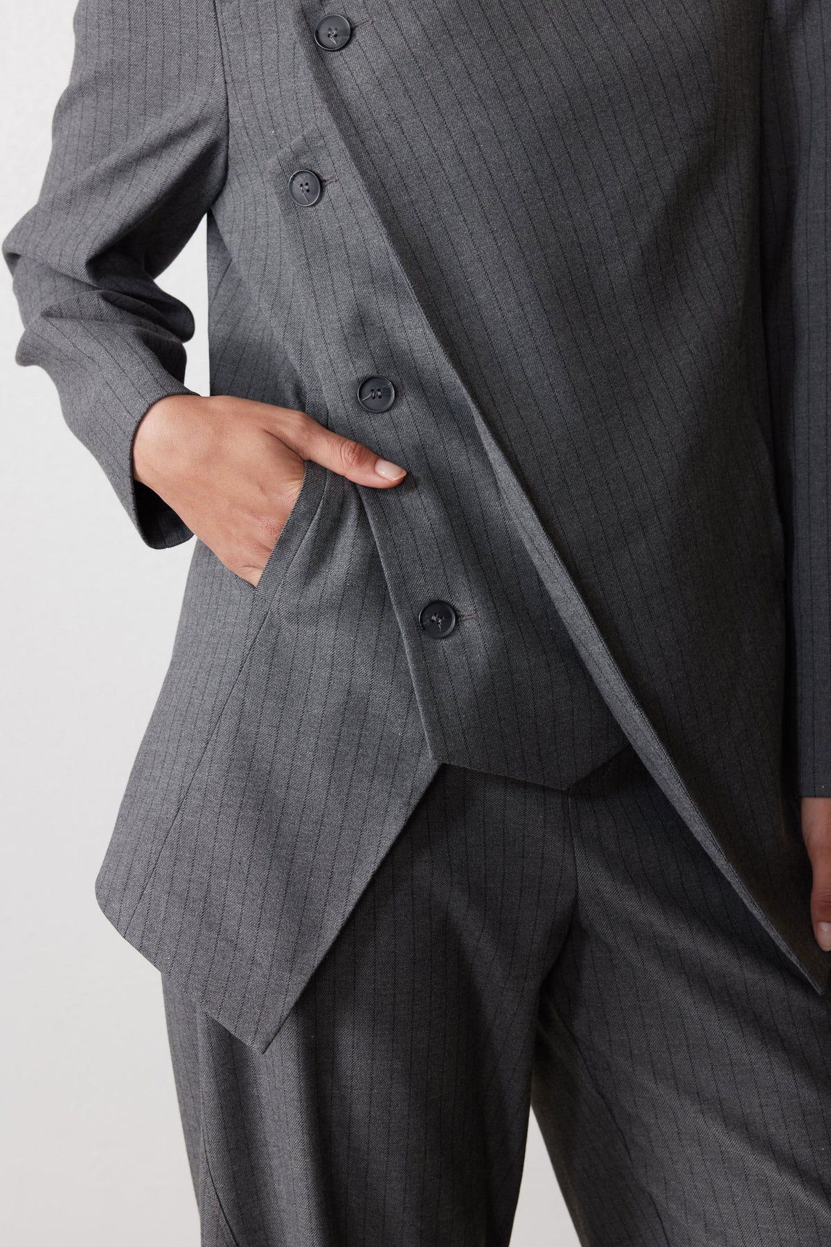 Gray pinstripe asymmetric suit jacket detail with buttoned flap and angled front panel