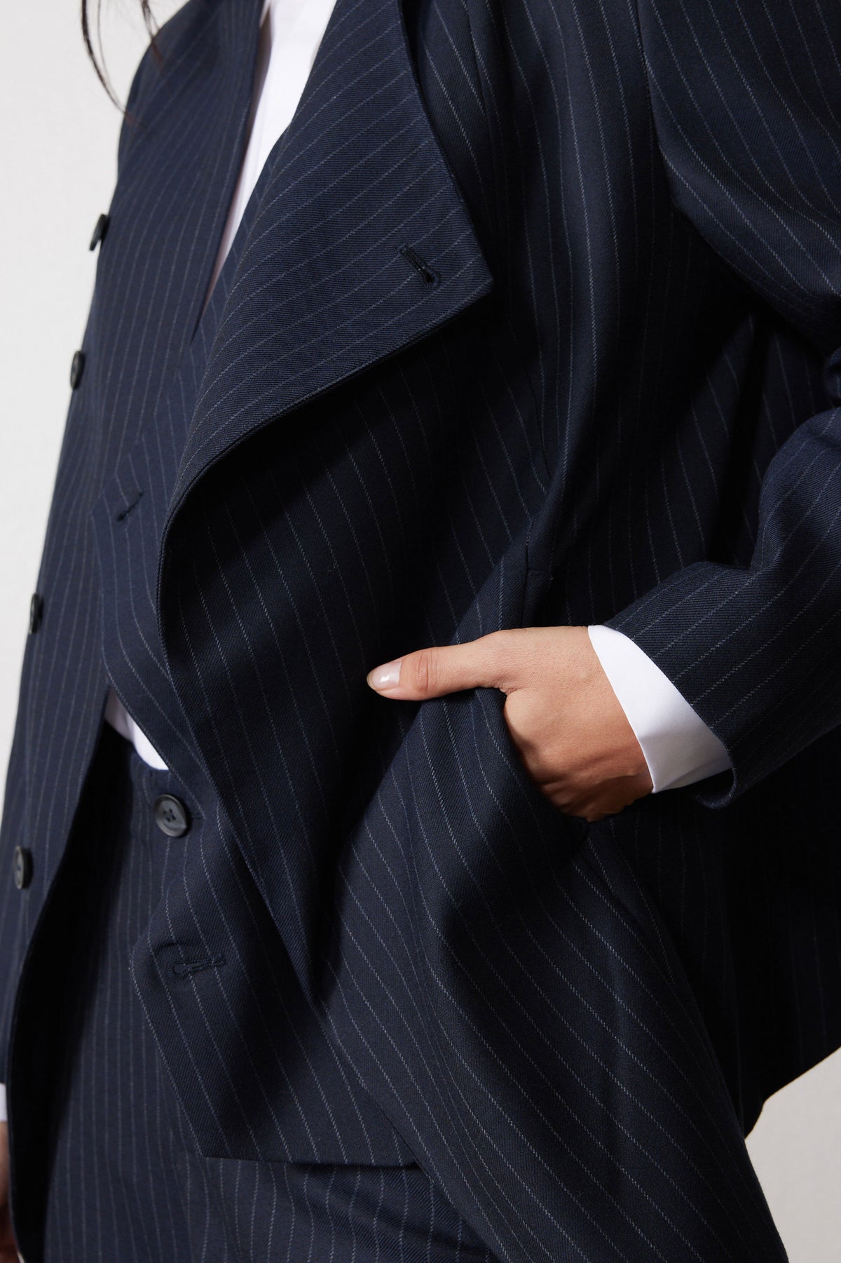 Navy pinstripe asymmetric jacket lapel and button placket, with welt pocket detail