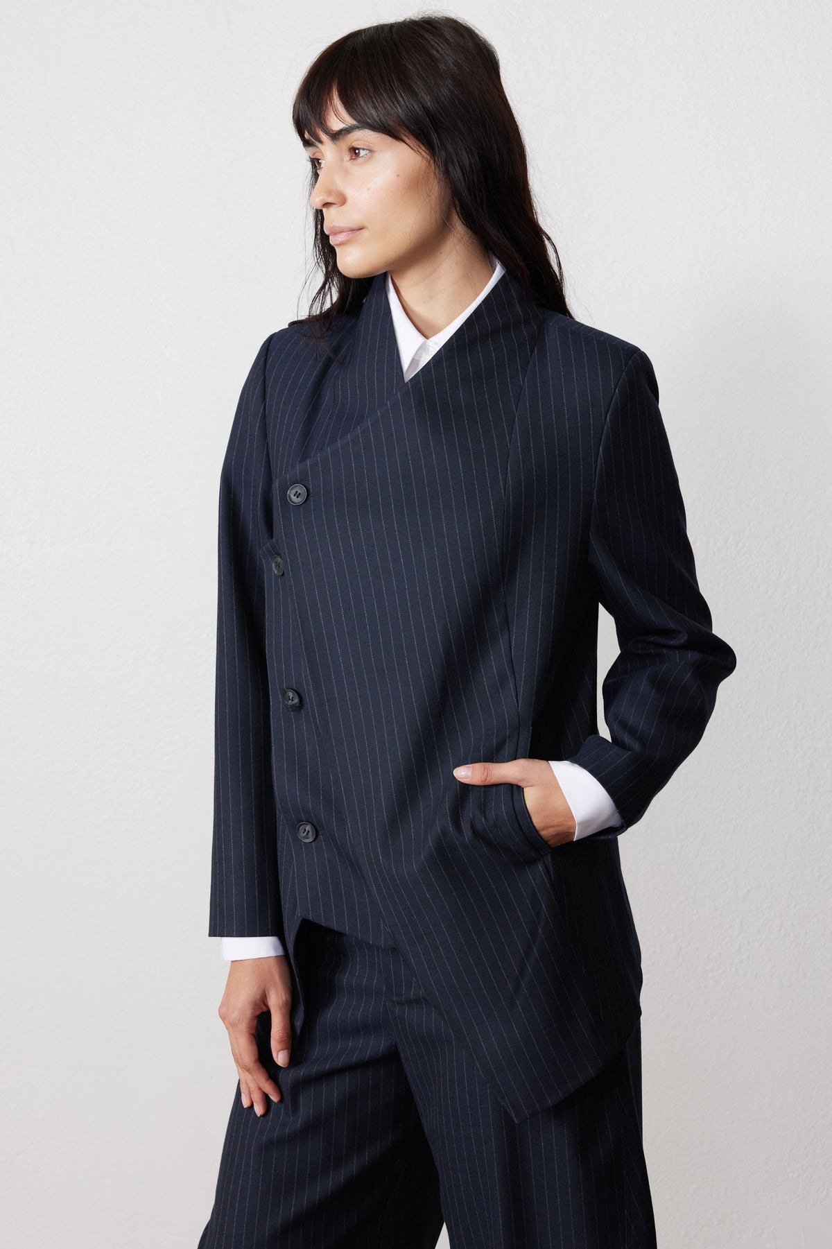 Navy pinstripe asymmetric suit jacket, side view, button closure and cuff detail