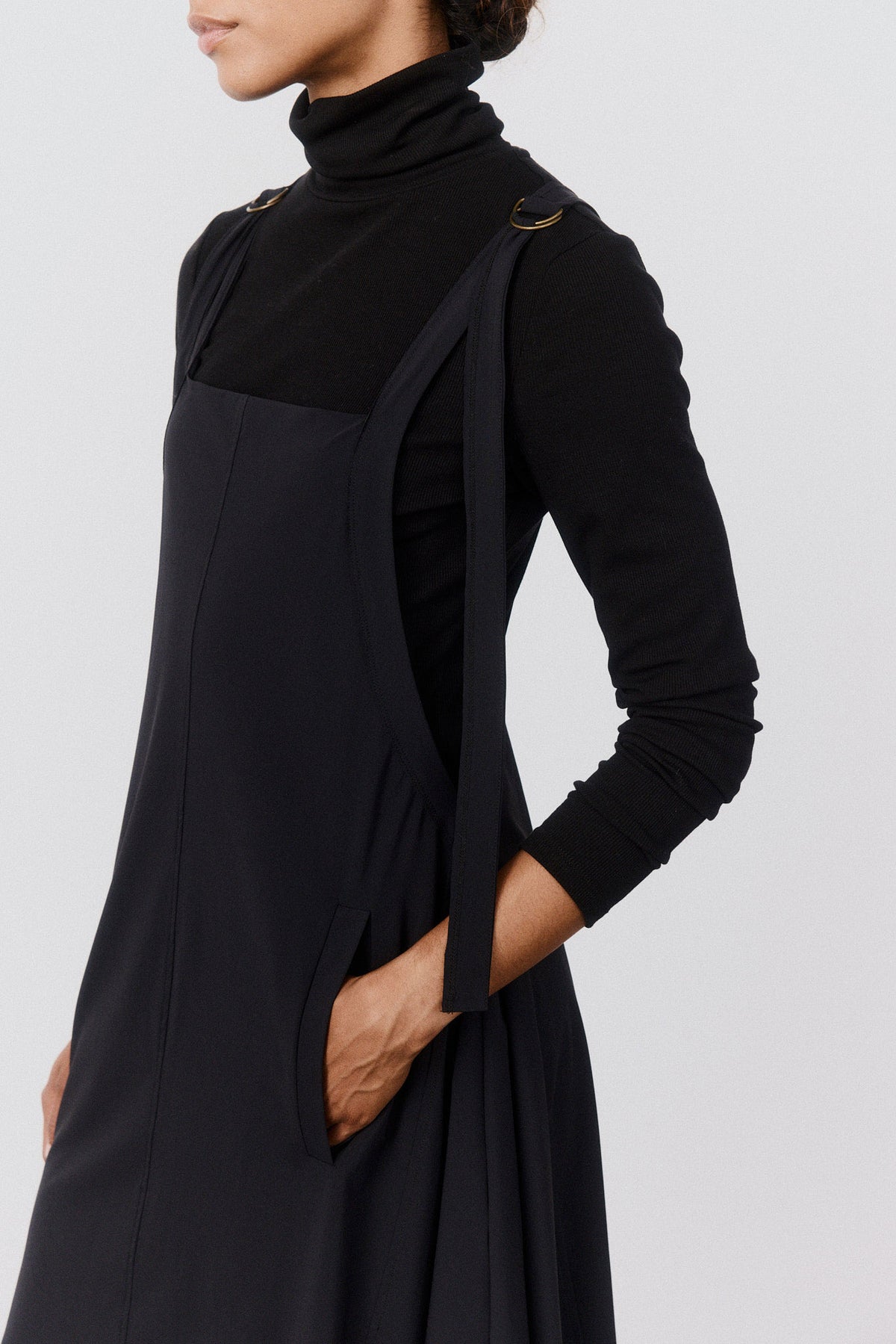 Black sarafan dress with diagonal front panel detail and asymmetrical draped skirt.