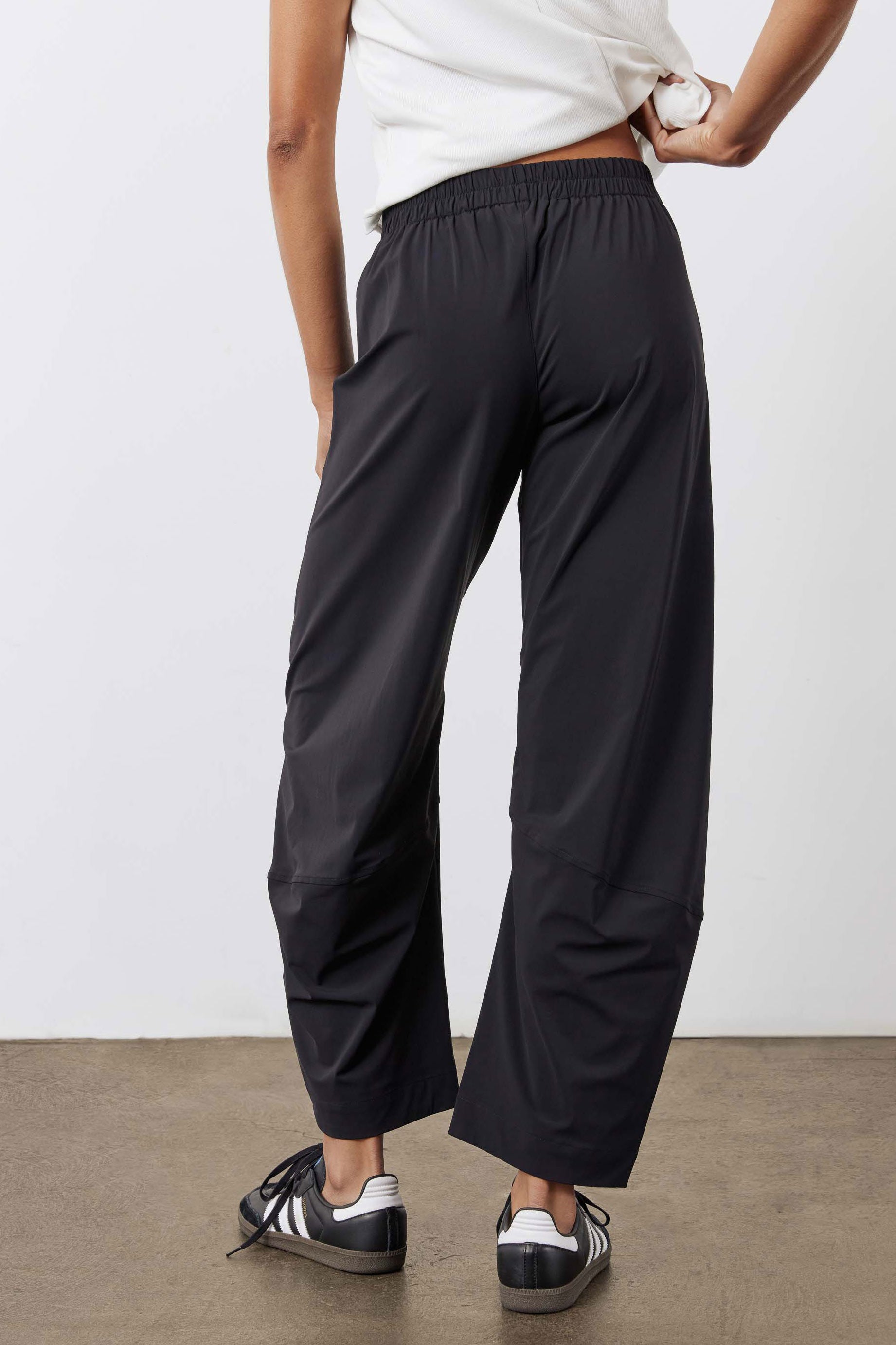 Black work pants with relaxed tapered wide legs and elastic waistband, walking side view