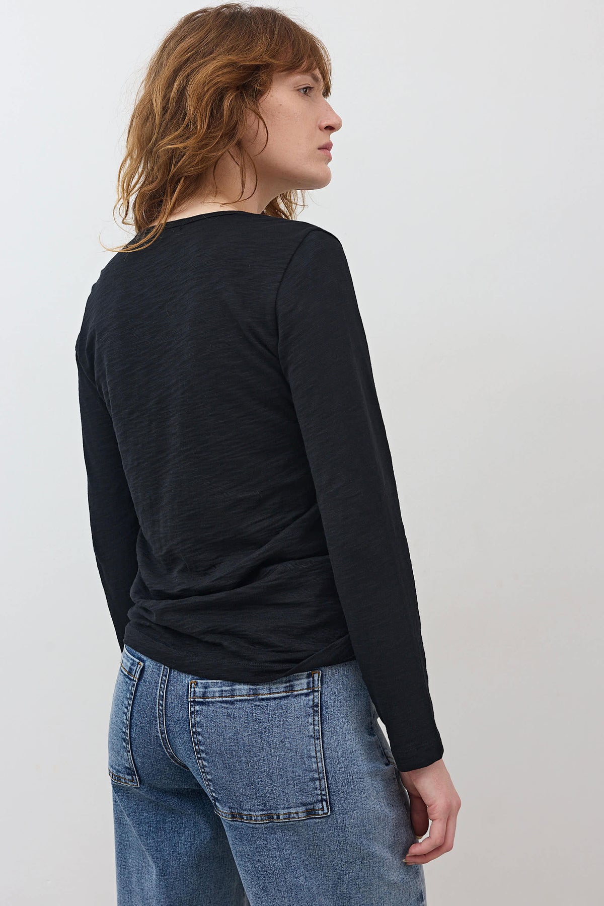 Black long-sleeve V-neck top in back view, smooth fabric with curved hem