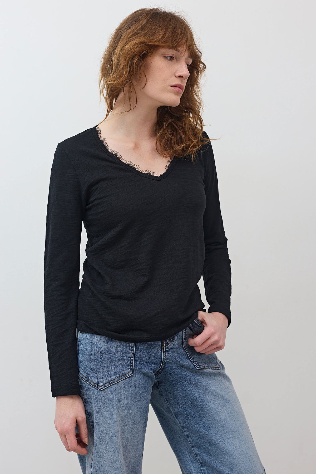 Black lace-trim long-sleeve V-neck top worn with jeans, side profile