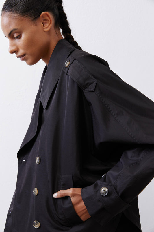 Black oversized nylon trench close-up with double row buttons and shoulder yoke detail.
