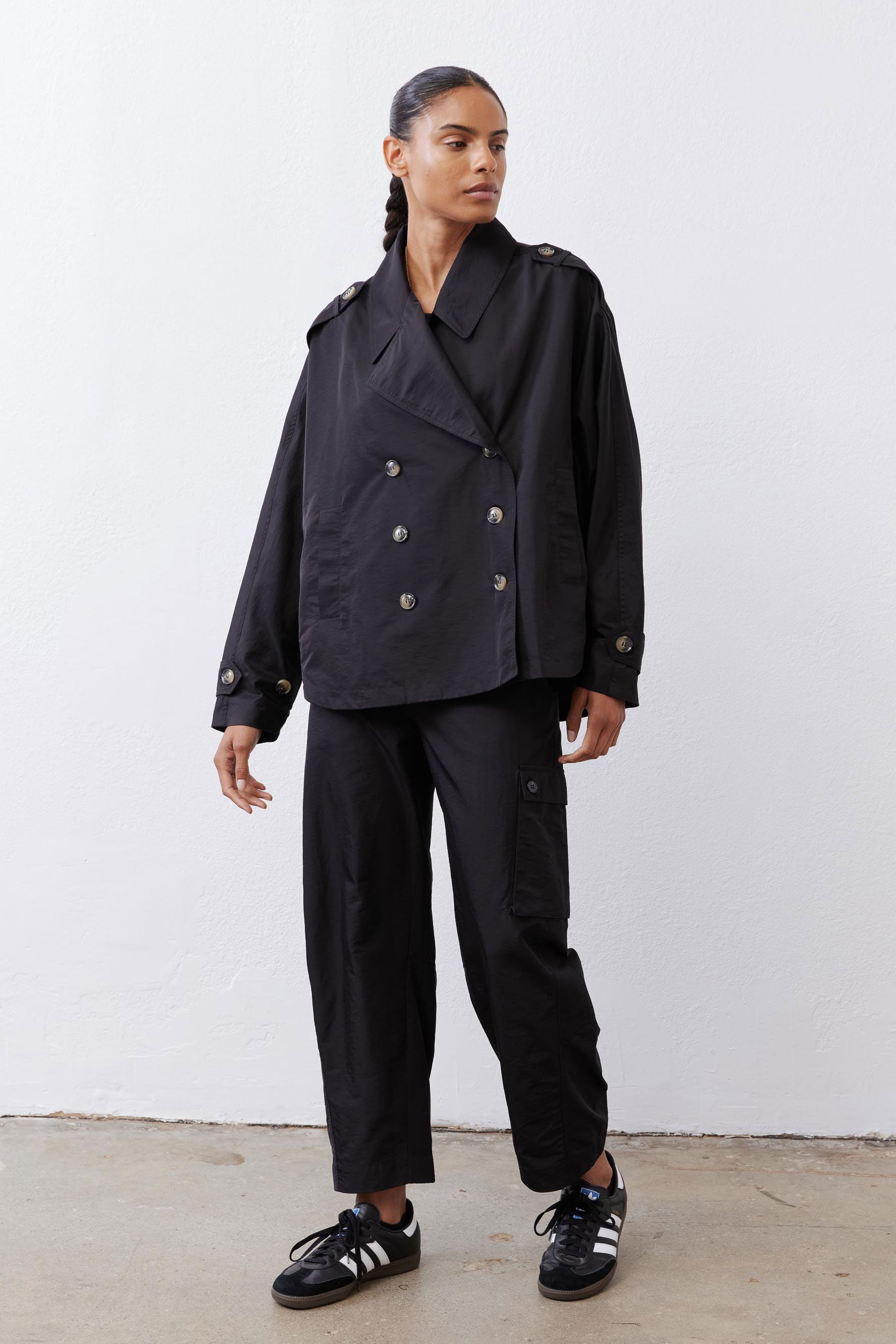 Black oversized nylon trench with double-breasted snaps and flap pockets, long sleeves.