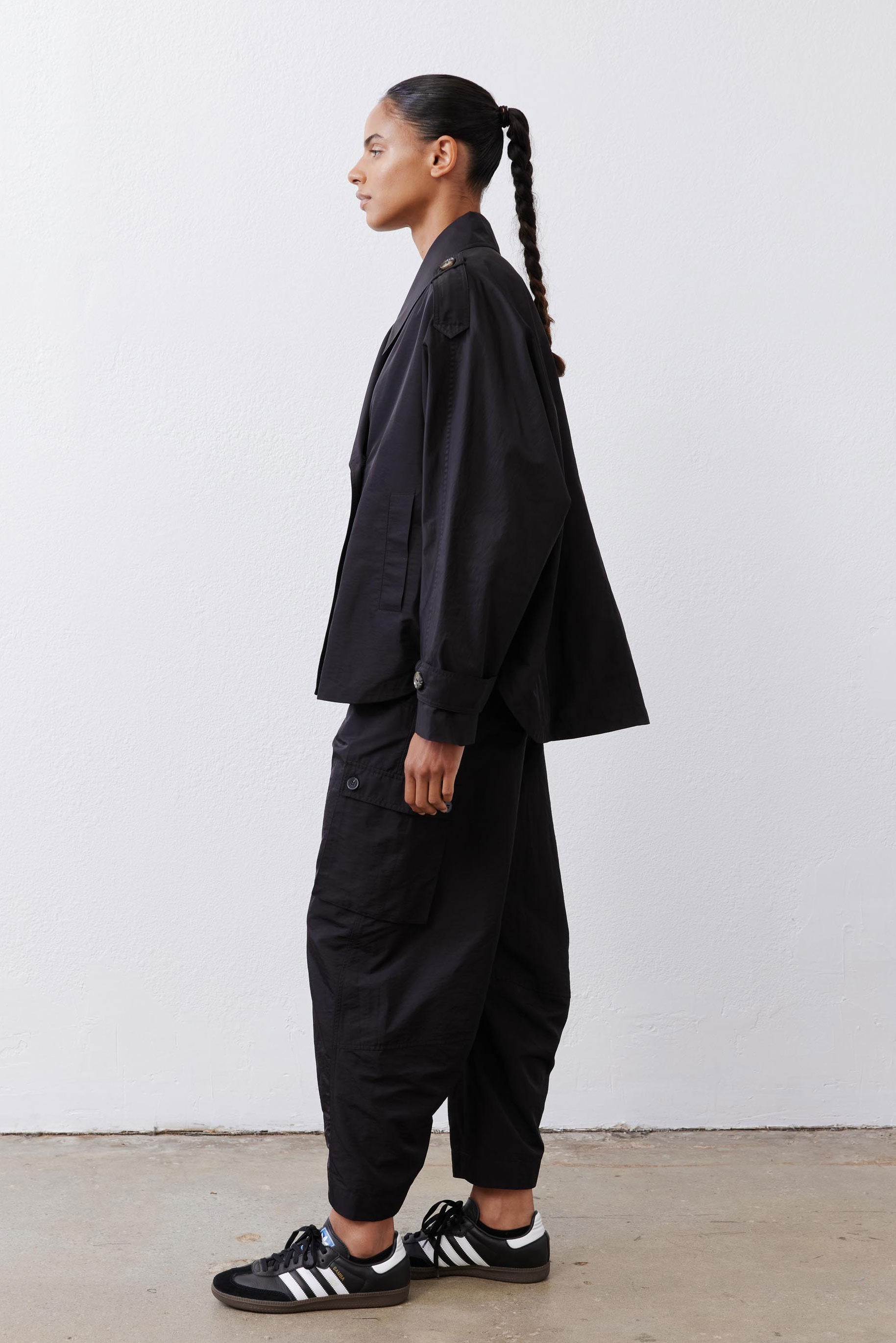 Black oversized nylon trench in side profile with relaxed fit and long hem.