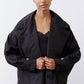 Black oversized nylon trench with button closure, notch lapels, and flap pockets.
