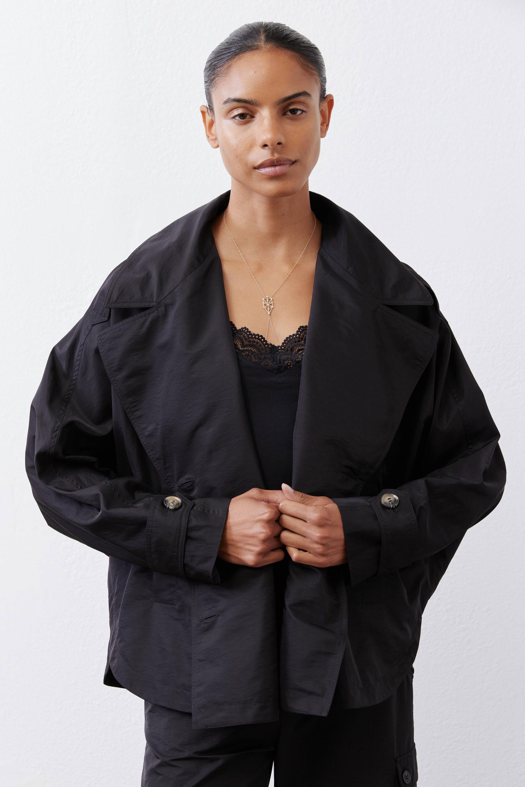 Black oversized nylon trench with button closure, notch lapels, and flap pockets.