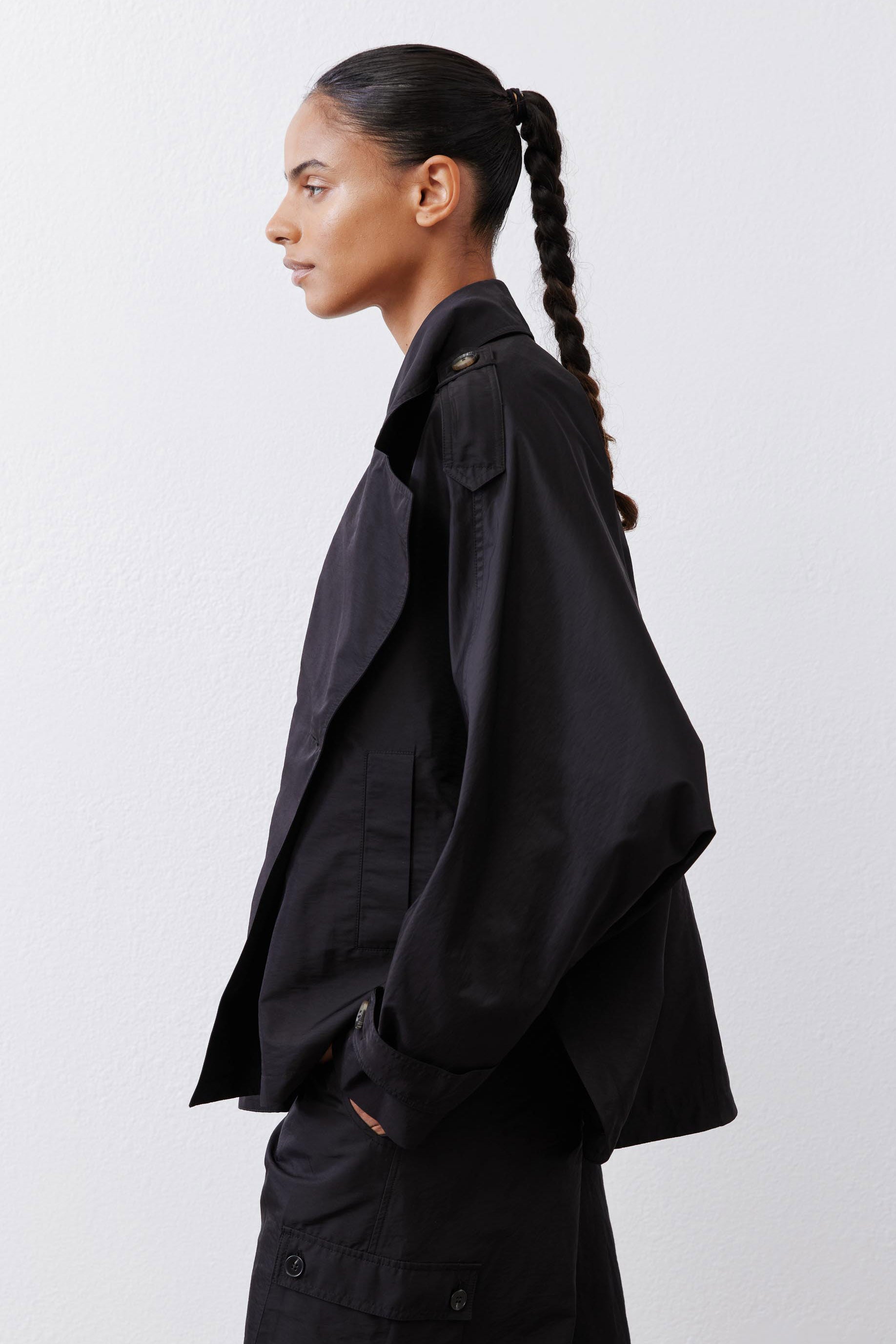 Black oversized nylon trench from side with large shoulder yoke and long cuffed sleeve.