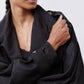 Black oversized nylon trench close-up with textured buttons, lapel collar, and pocket flap.