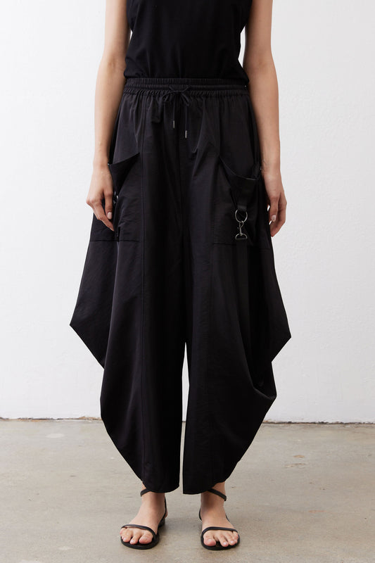 Black wide-leg parachute pants with elastic drawstring waist, draped legs, metal ring