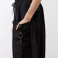 Black parachute pants close-up of side pocket with ring hardware and drawstring.