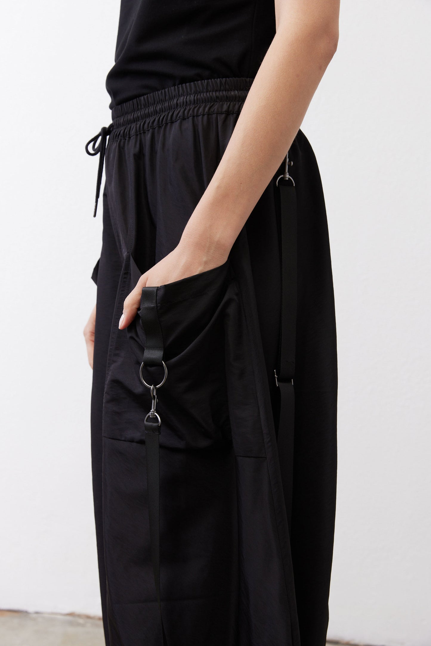 Black parachute pants close-up of side pocket with ring hardware and drawstring.