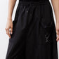 Black parachute wide-leg pants close-up: elastic waist, drawstring ties, side pocket rings.