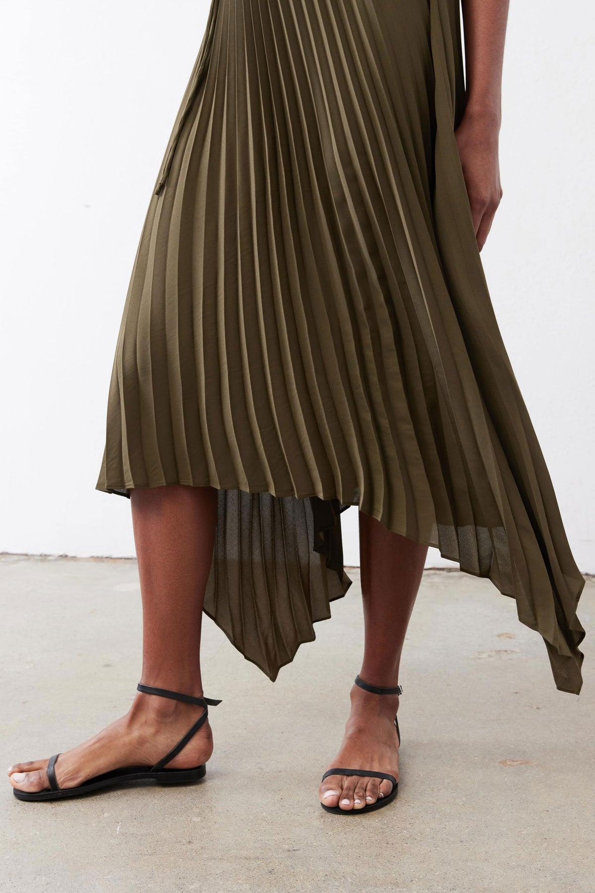 Olive pleated wrap dress showing layered asymmetrical hem and pleated skirt.
