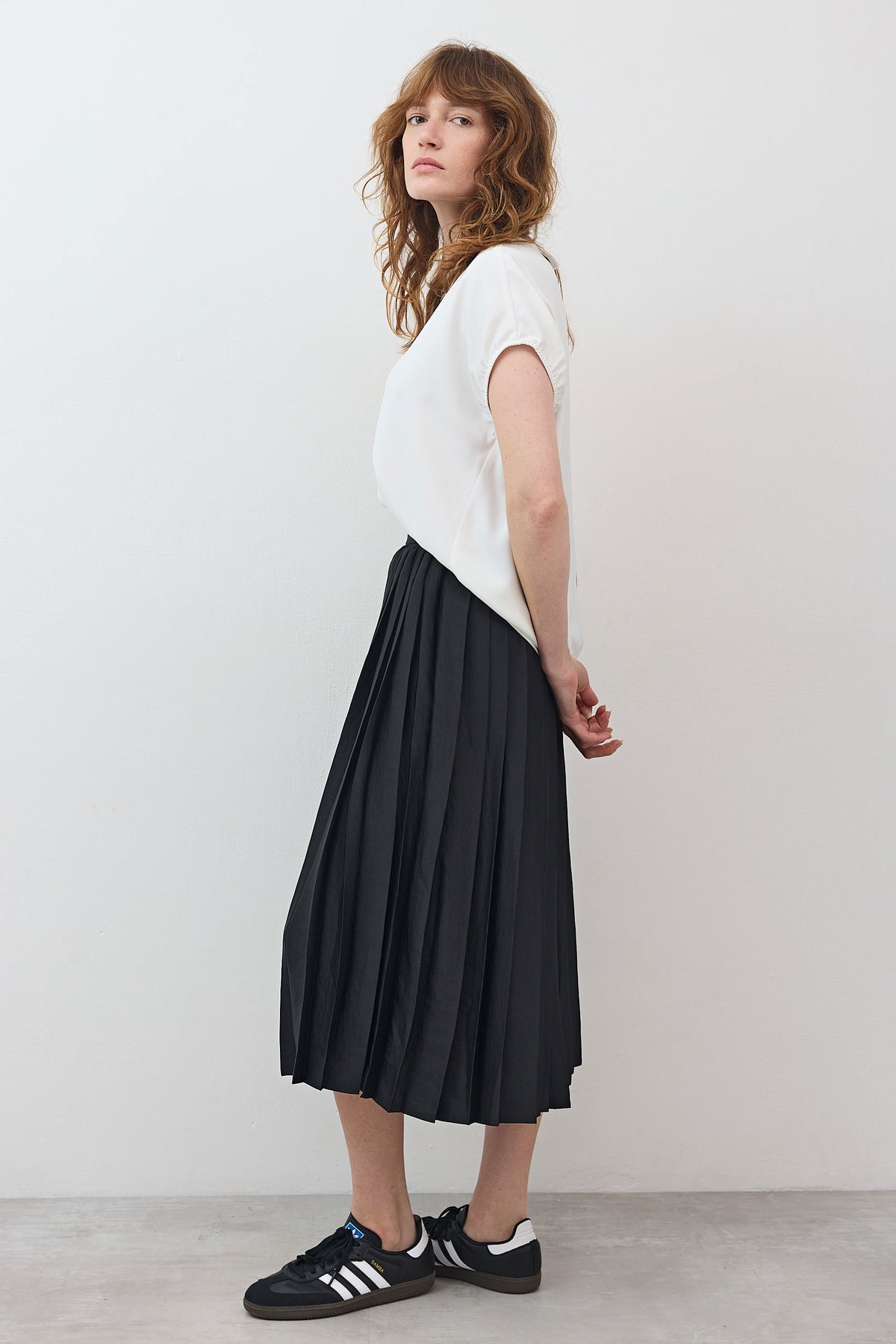 Black pleated pull-on skirt with elastic waistband, mid-calf length, side profile