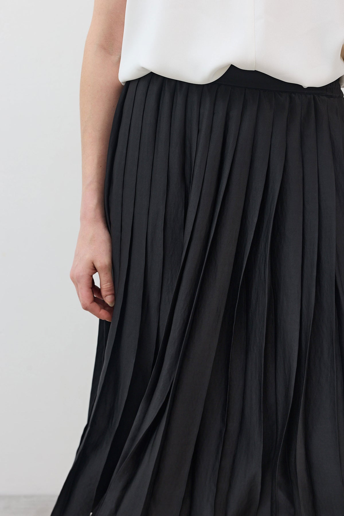 Black pleated skirt close-up showing vertical pleats and wide elastic waistband