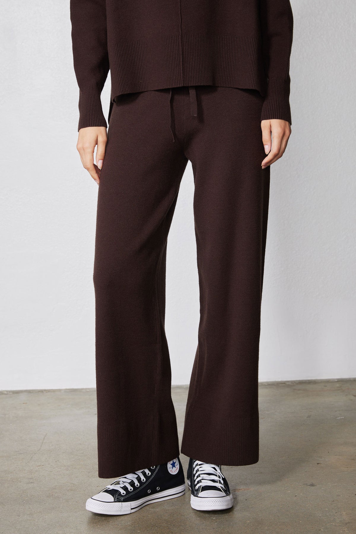 Chocolate plum wide-leg drawstring pants with sneakers, full lower-body view