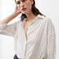 White tunic with black dot pattern, open collar, and long sleeves gathered at cuffs