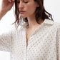 White tunic close-up with small black dots, open collar, and buttoned front