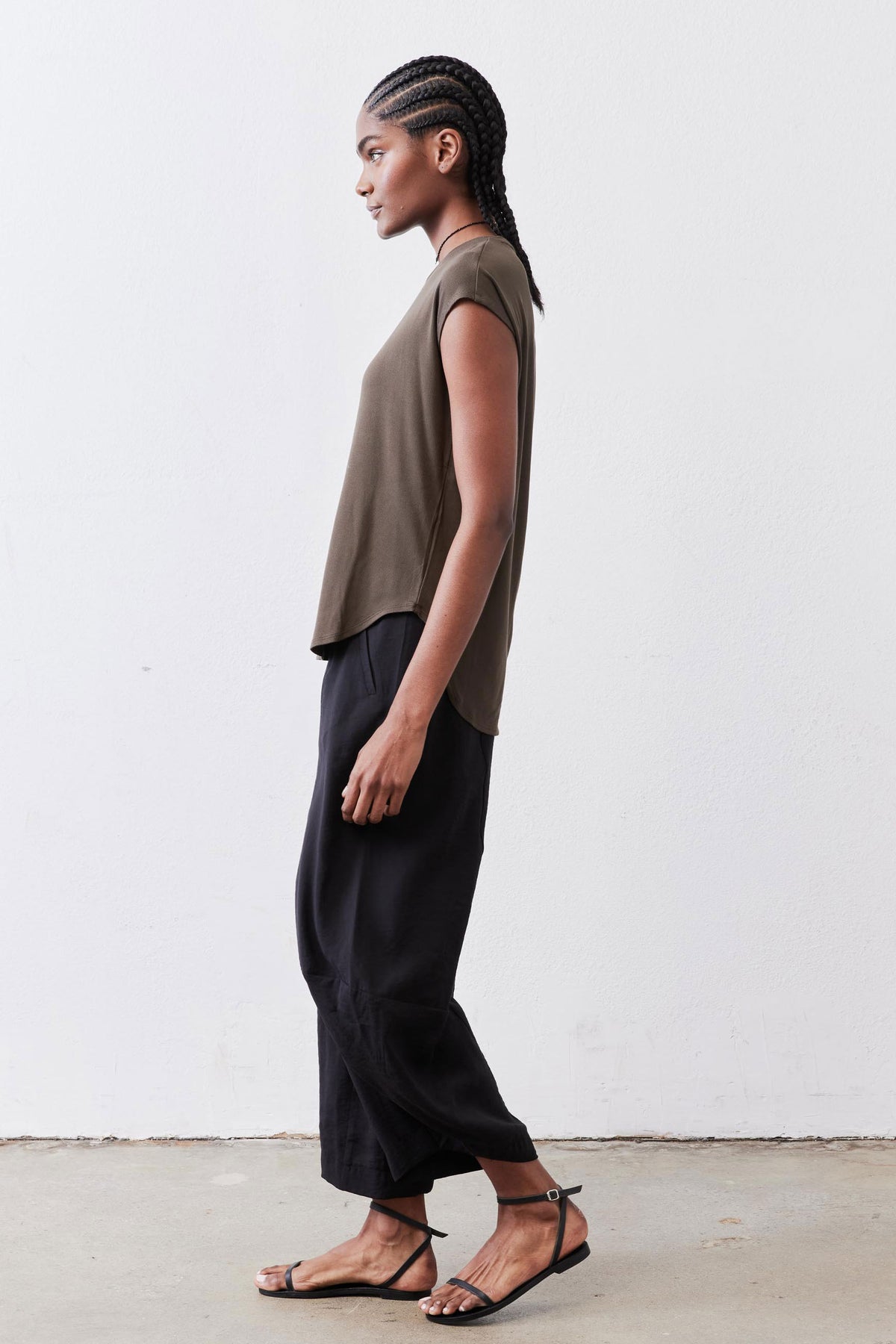 Olive crewneck short-sleeve tee, profile view with curved hem over dark pants