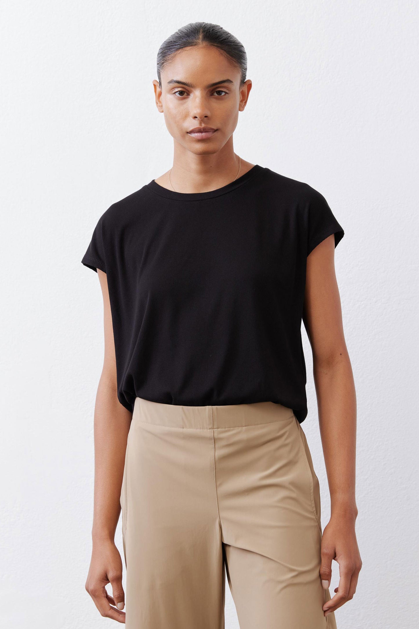 Black tuck-in tee with crew neck and short sleeves, worn with beige pants