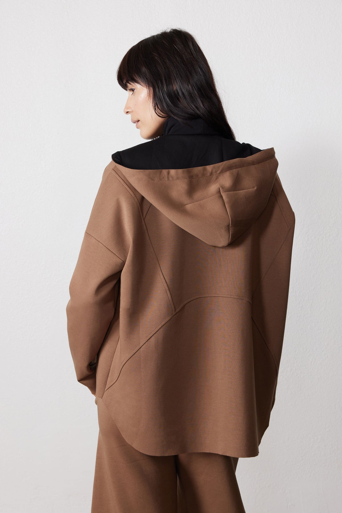 Back view of a mocha scuba hoodie with a draped hood and curved seam detailing.