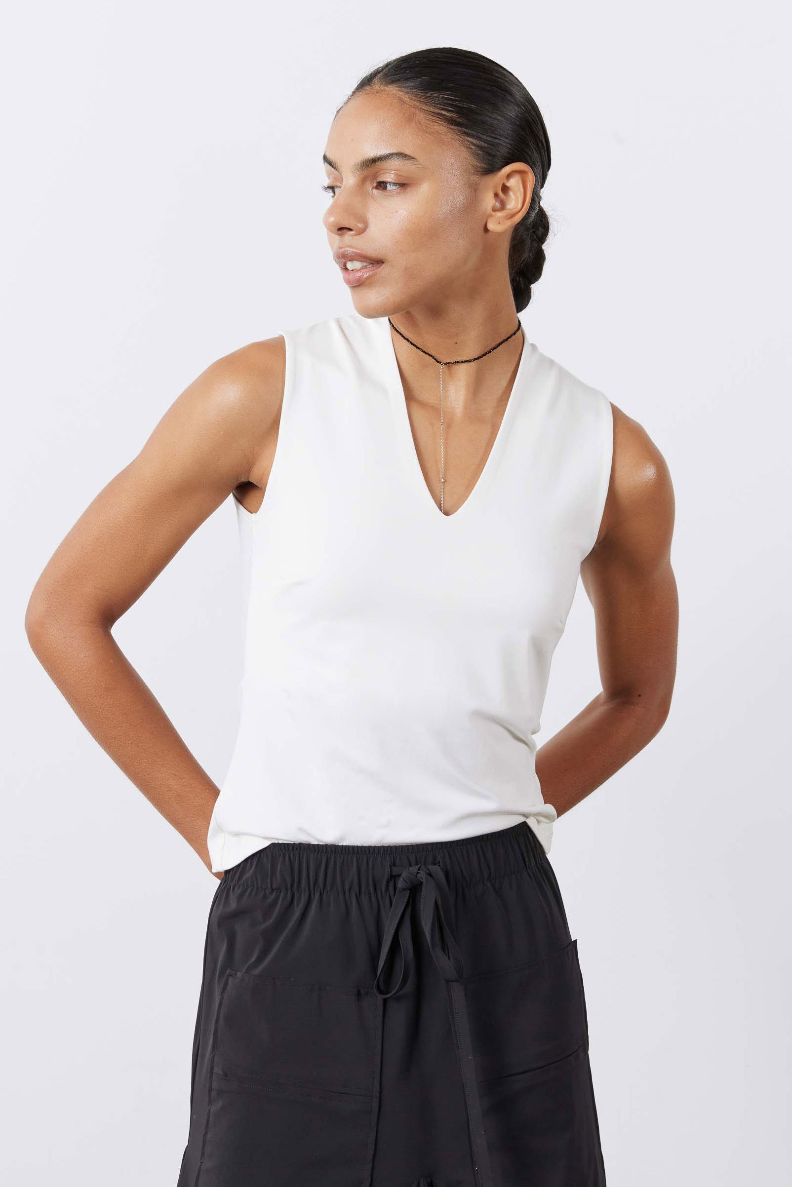 White sculpted V-neck tank top, sleeveless fitted silhouette, model side view