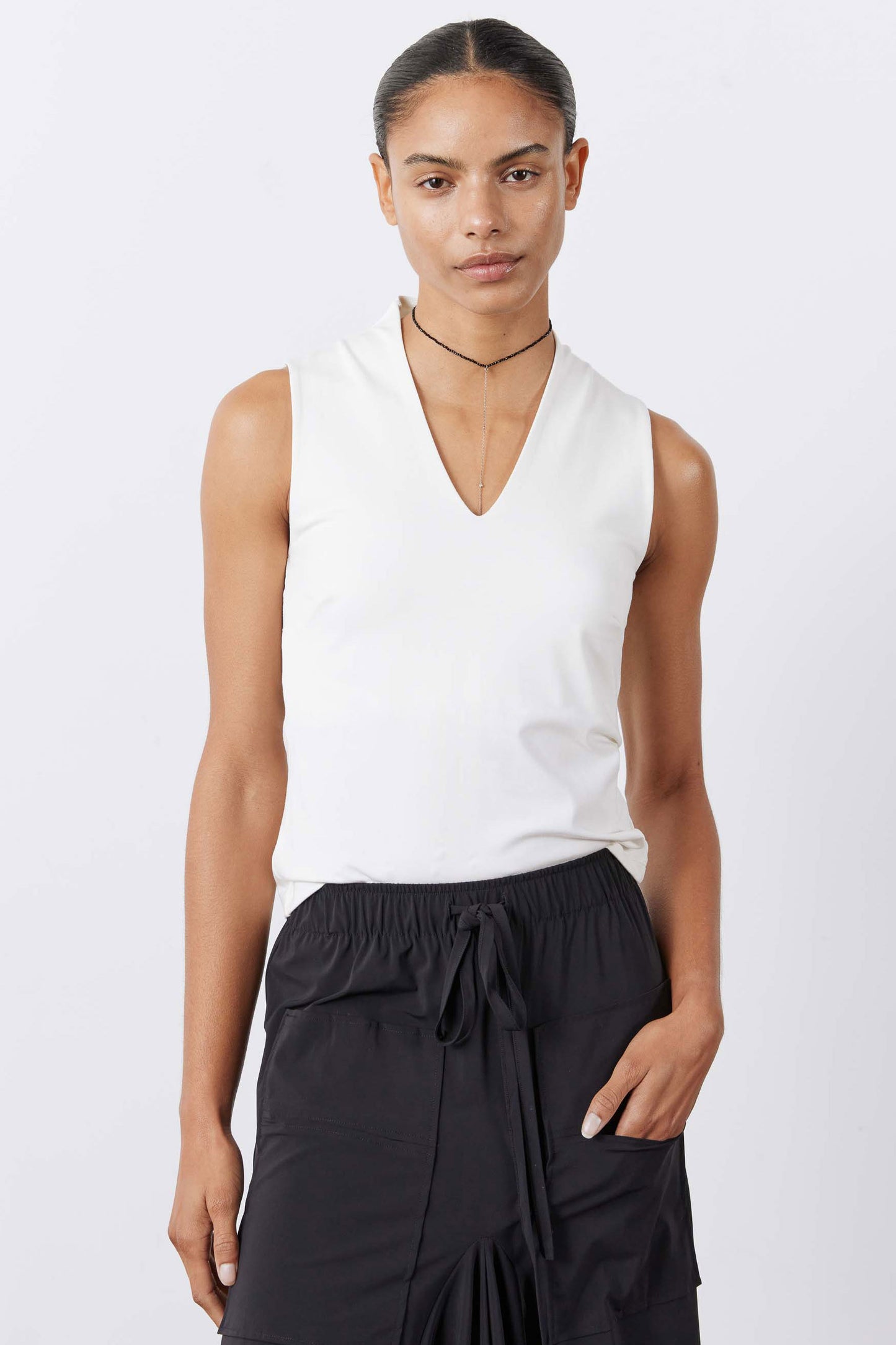 White sculpted V-neck tank top on model, sleeveless with fitted drape