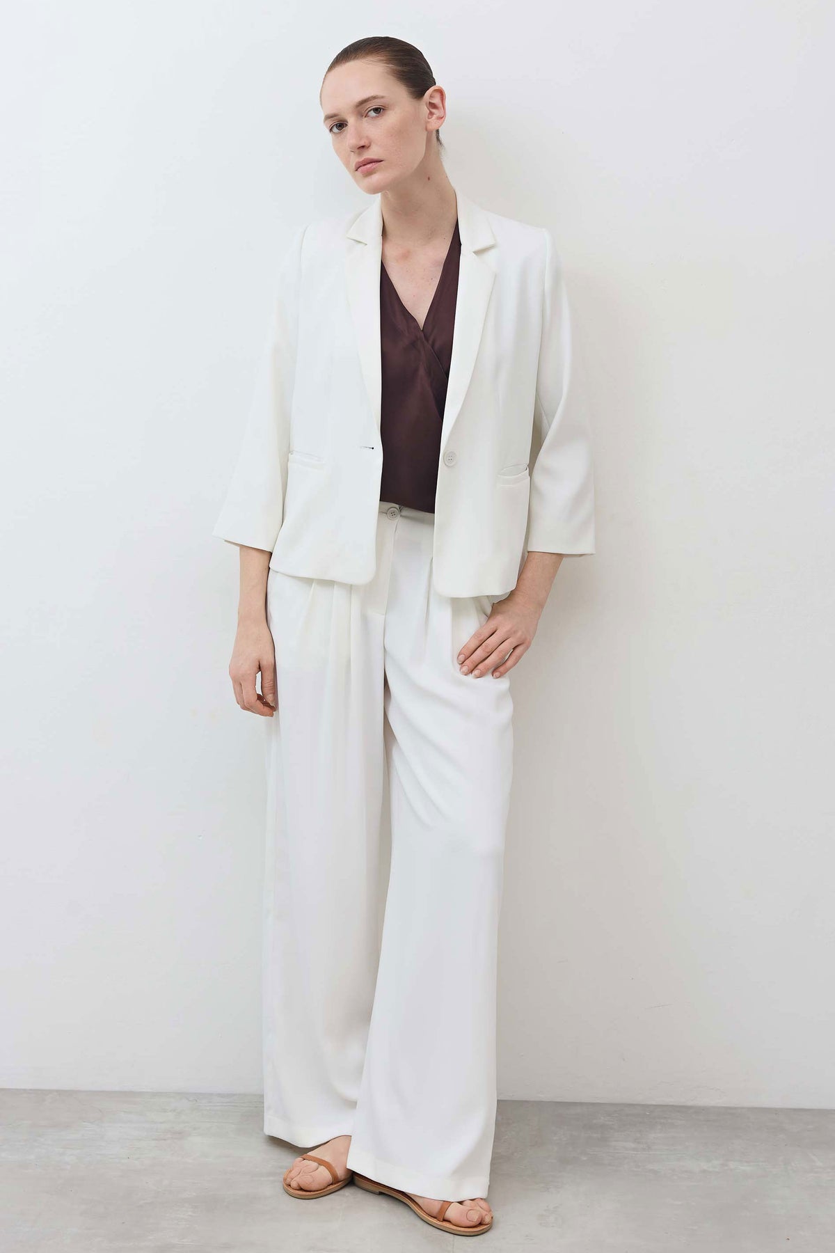 White shrunken blazer worn open, three-quarter sleeves, notch lapel and chest pocket.