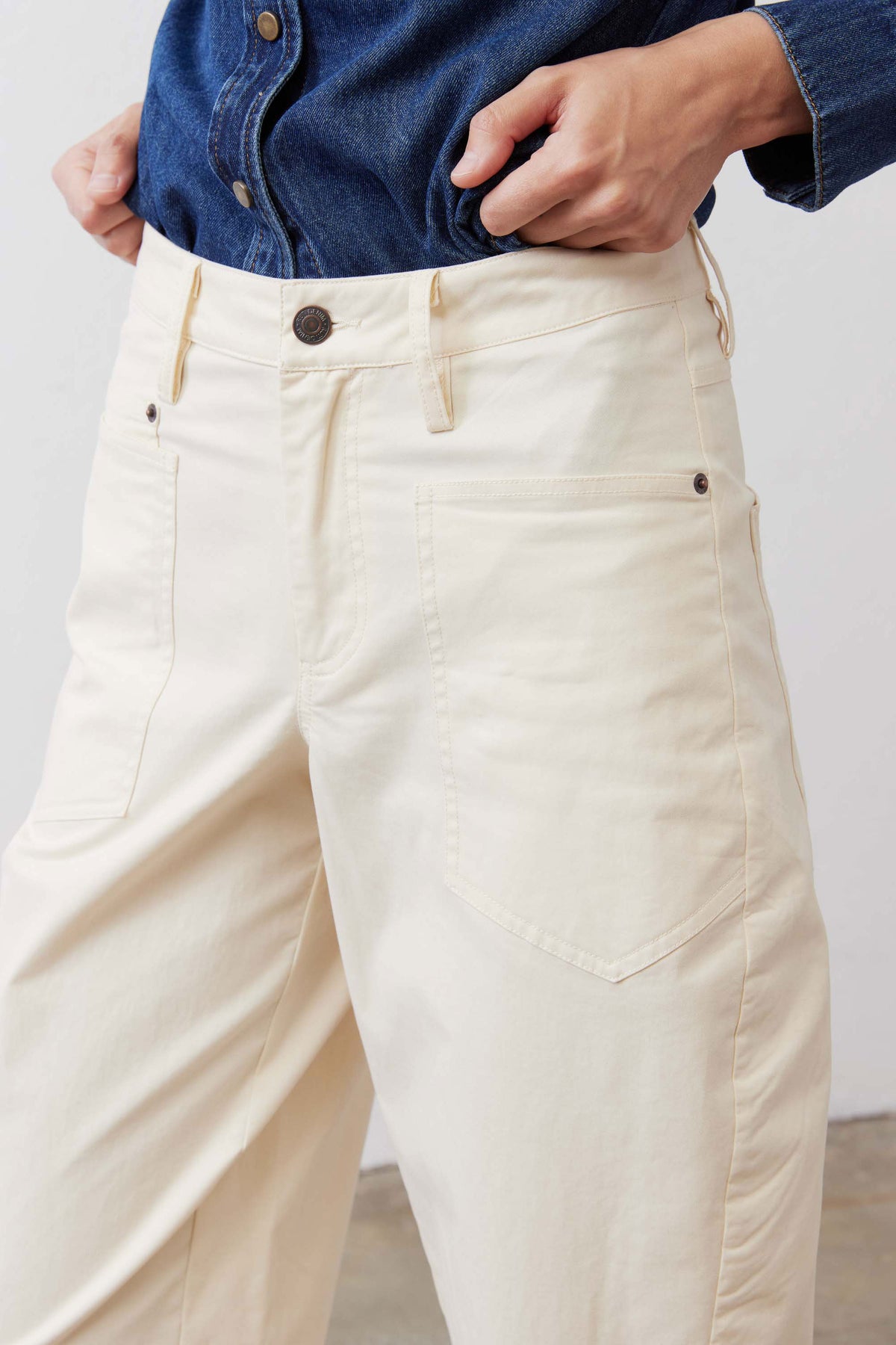 Ecru twill pants detail: button closure, belt loops, and side pocket stitching