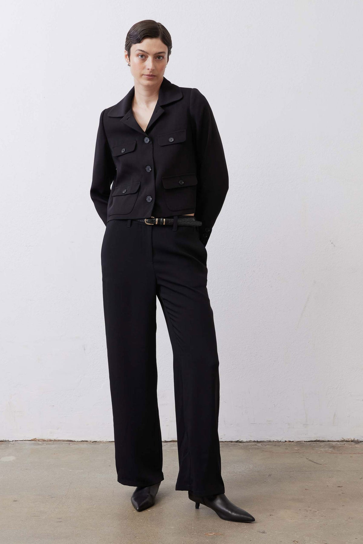 Black collared classic jacket with long sleeves, button front, flap pockets, and matching belt