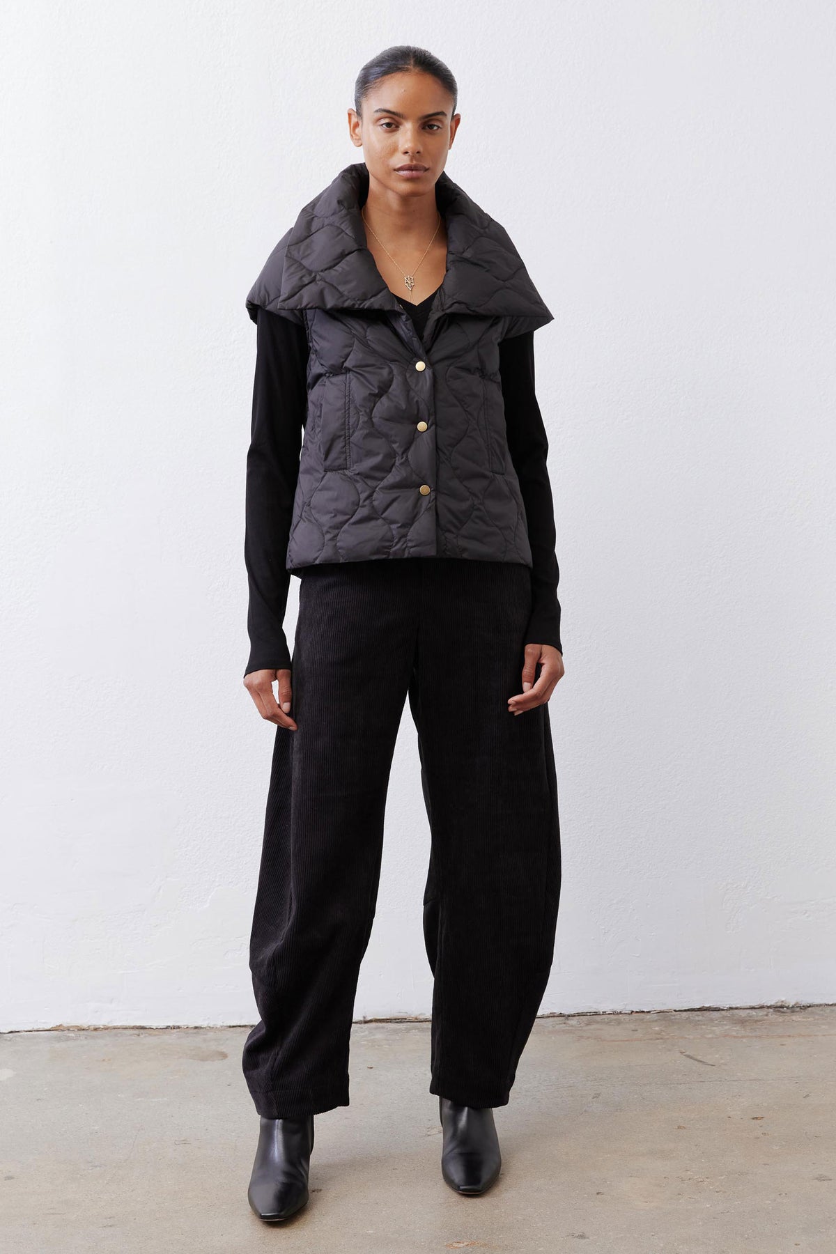 Black quilted down vest with stand collar and gold snap buttons