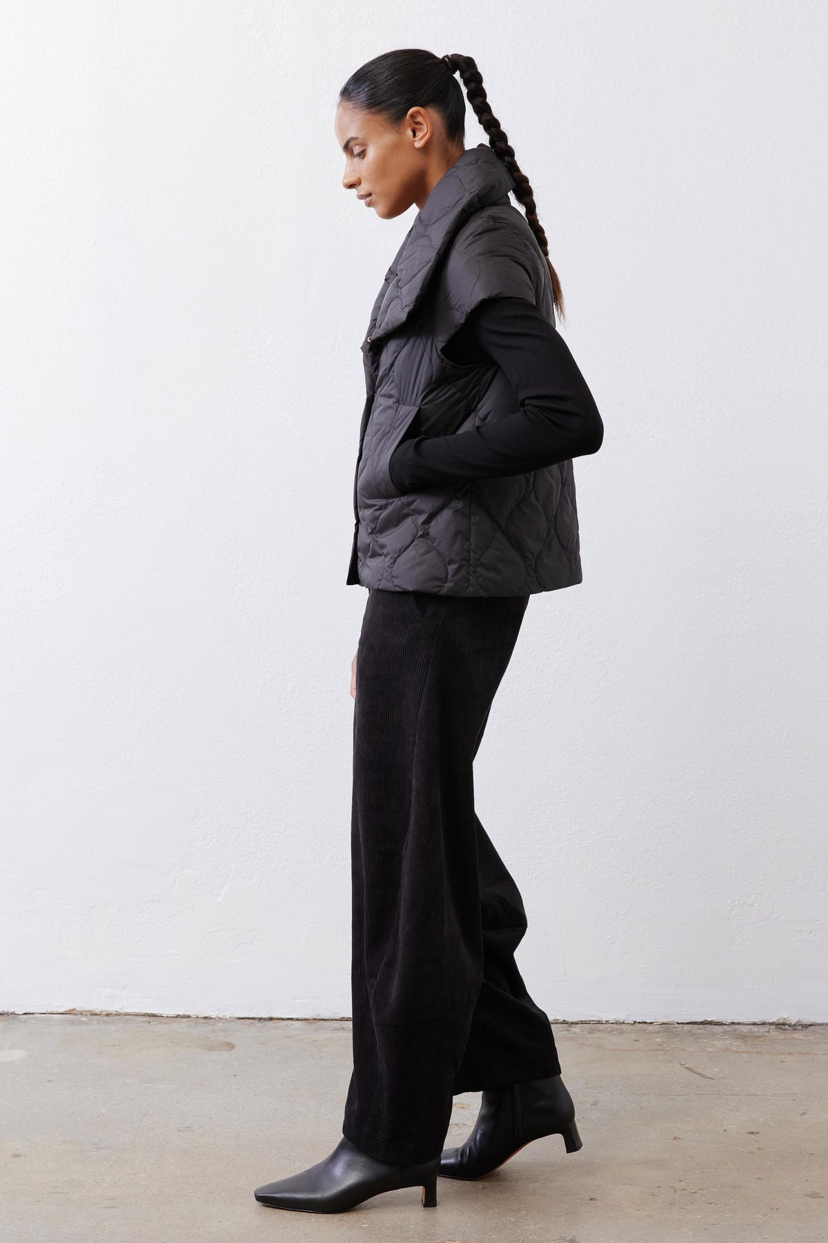 Black quilted down vest, side view, with stand collar and snap buttons